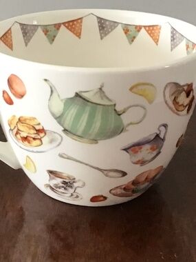 A modern ceramic mug with watercolor illustrations of tea-time treats.